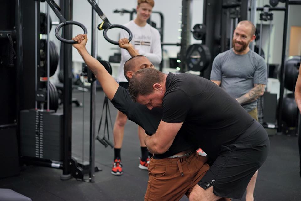 Coach demonstrating a single-arm ring pull-up technique to a workshop attendee