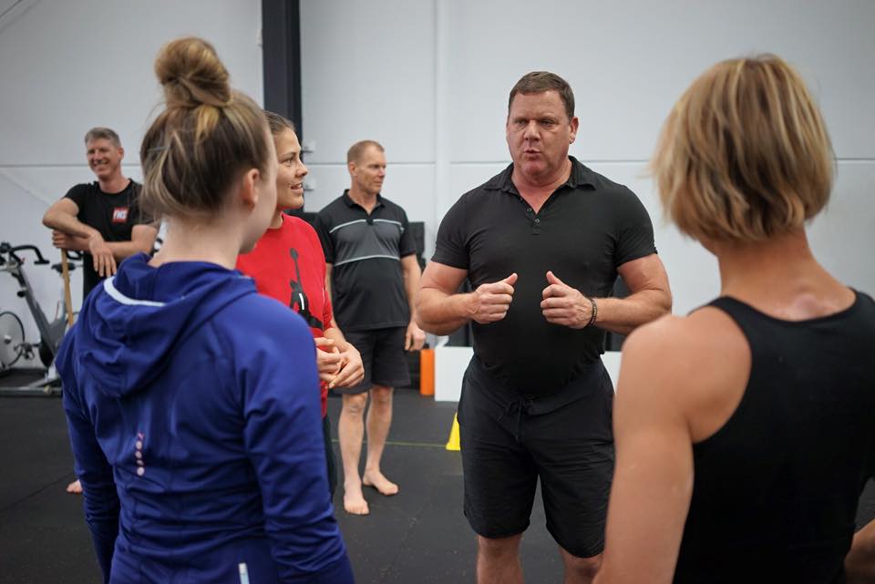 Coach Dan John speaking with a small group of athletes in a gym